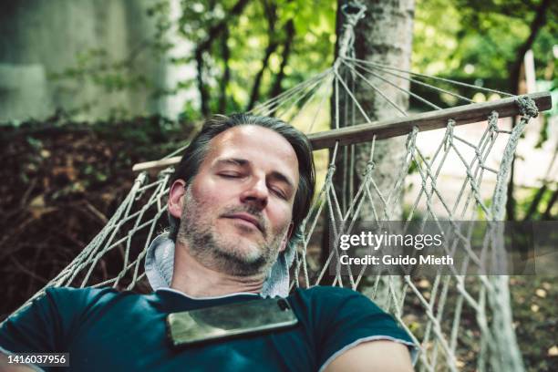 mature man sleeping in hammock with mobile phone on his chest. - zurücklehnen stock-fotos und bilder