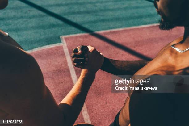 two multiracial friends athletes with different skin tone holding hands as the symbol of teamwork and support - gratitude symbol stock pictures, royalty-free photos & images