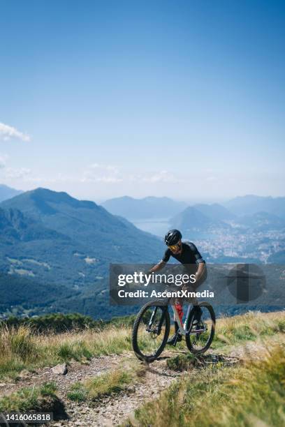 athlete rides e-mountain bike on trail above mountains - mountain bike stock pictures, royalty-free photos & images