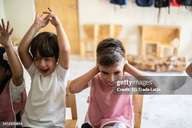 students celebrating and boy covering his ears in the classroom at school - boom for real stock pictures, royalty-free photos & images