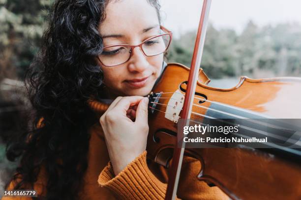 curly brunette woman with glasses tuning her violin with its fine tuner, outdoor in the field. - stringed instrument stock pictures, royalty-free photos & images