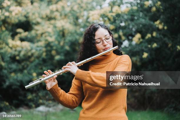 curly brunette woman with glasses playing transverse flute outdoor in nature - 木管楽器 ストックフォトと画像