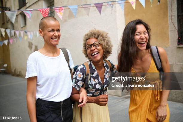 three happy interracial female friends smiling while enjoying a walk together outdoors on the street. - hair loss in woman stock pictures, royalty-free photos & images