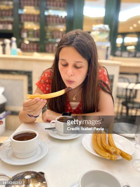 young woman eating churros with chocolate - churro stockfoto's en -beelden