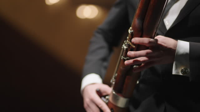 man is playing bassoon in brass orchestra, closeup view of hands of bassoonist, musician is using wind instrument