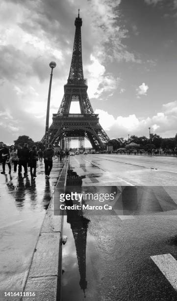 view of the eiffel tower with its reflection on the wet street in paris - atmosferische lucht stockfoto's en -beelden