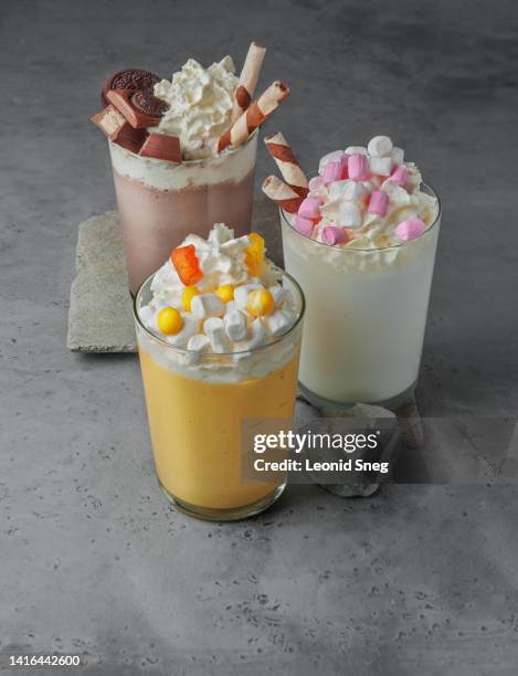 various milkshakes with toppings and whipped cream on gray background - chocolate bar foto e immagini stock