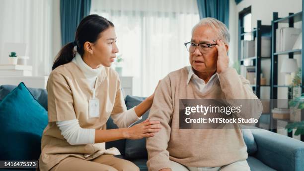 junge asiatische weibliche professionelle pflegekraft kümmern sich um die beruhigung kranker älterer männlicher patienten im wohnzimmer zu hause. - nurse with old male patient home care stock-fotos und bilder