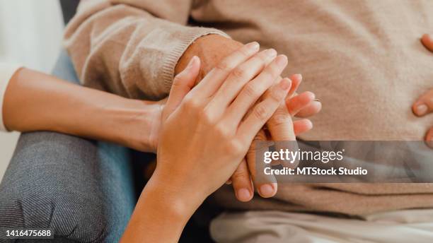 close-up young asian female caregiver hold old male hand take care elderly patient on wing chair at home. - die imagens e fotografias de stock