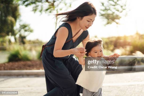 young asian mother assisting her baby girl to walk at the park. - chinese mothers day - fotografias e filmes do acervo