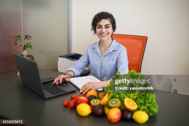 portrait of beautiful smiling nutritionist looking at camera and showing healthy vegetables in the consultation - healthy workplace stock pictures, royalty-free photos & images