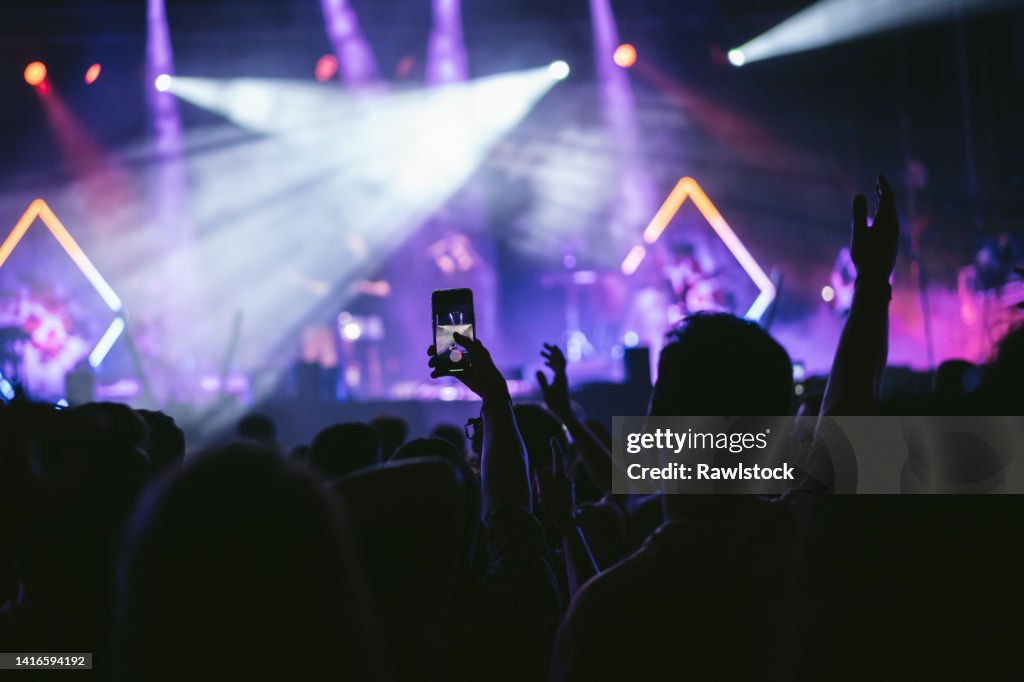 Group of unrecognizable people enjoying a music concert while one of them takes a picture with his cell phone.
