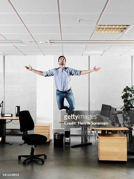 young businessman floating above the desk - levitación fotografías e imágenes de stock