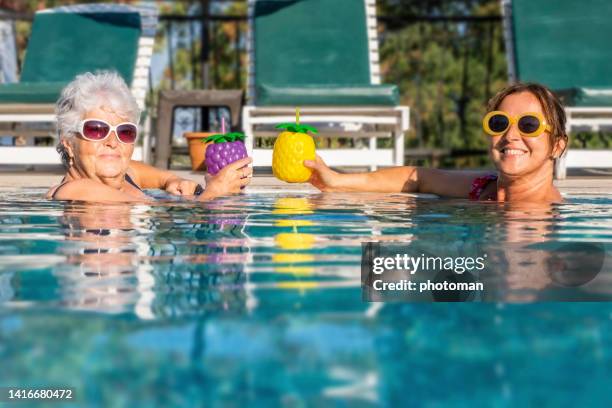 dos mujeres en la piscina sonriendo mirando a la cámara disfrutando de cócteles - mothers day beach fotografías e imágenes de stock