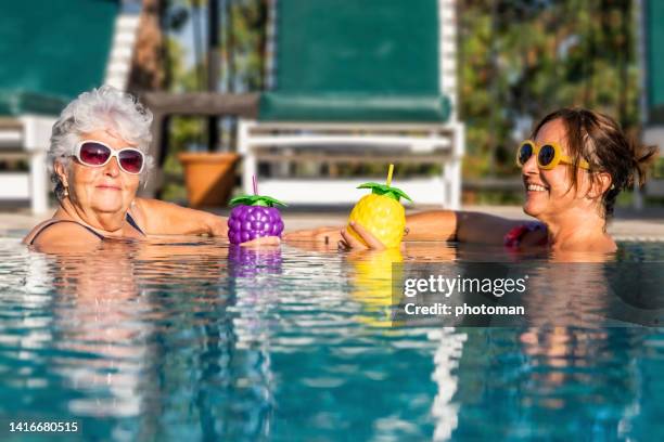 dos mujeres felices en la piscina sonriendo y disfrutando de cócteles - mothers day beach fotografías e imágenes de stock