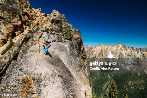 a woman climbs along a dramatic ridge line high up on a mountain - evasion fiscale stockfoto's en -beelden