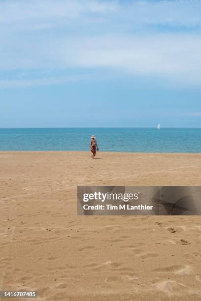 mixed race woman walking on beach with horizon in background - blue white summer hat background stock pictures, royalty-free photos & images