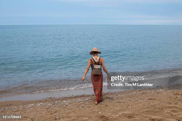 mixed race woman walking on beach with horizon in background - blue white summer hat background stock pictures, royalty-free photos & images