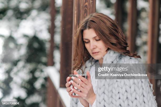 cute young caucasian teenage woman in beige fur coat, hat with pompon, scarf and white mittens holding steaming white cup of hot tea or coffee, outdoor in sunny winter day. bask in the cold - woman hands in mittens stock-fotos und bilder