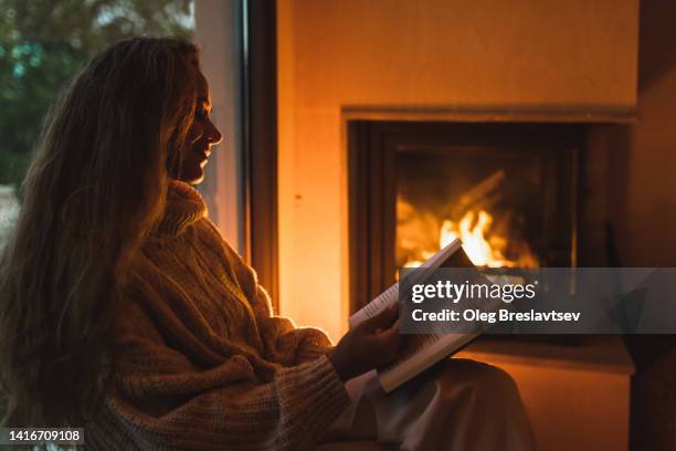 silhouette of smiling woman in woolen sweater reading book at home near fireplace. cozy evening - log fire stock pictures, royalty-free photos & images