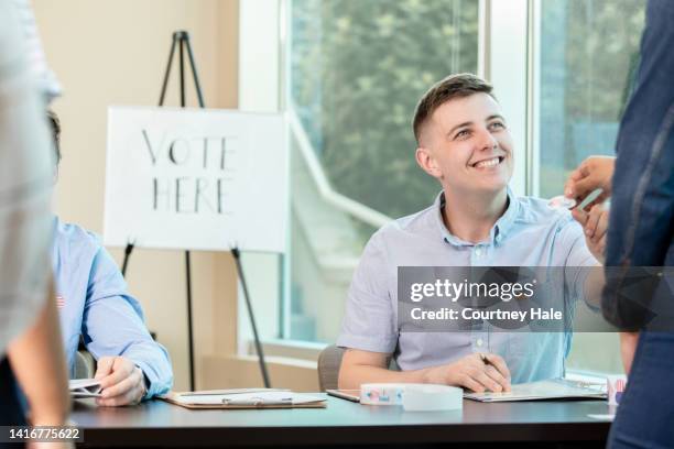 jovem adulto voluntário sorrindo enquanto devolve o cartão de identificação do eleitor. - voter registration - fotografias e filmes do acervo