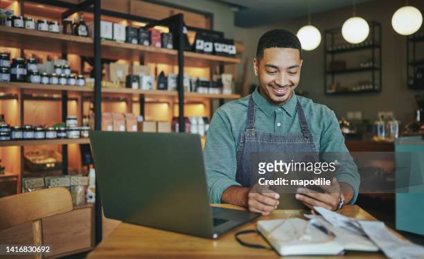 smiling deli manager working on a tablet and laptop in his shop - small business stock pictures, royalty-free photos & images