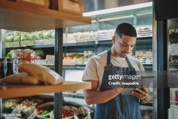 deli owner with a tablet checking inventory in his store - groceries tablet stock pictures, royalty-free photos & images