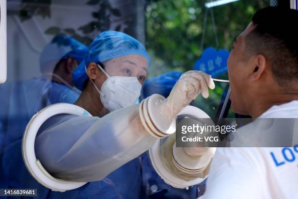 Medical worker in a COVID-19 nucleic acid testing cabin takes swab sample from a resident for COVID-19 nucleic acid test on August 22, 2022 in...