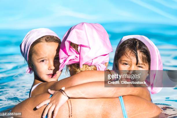 female breast cancer survivor with her daughters in the pool, all three wearing the pink scarf to fight breast cancer, both looking at the camera. concept of disease, chemotherapy and success. - best bosom fotografías e imágenes de stock