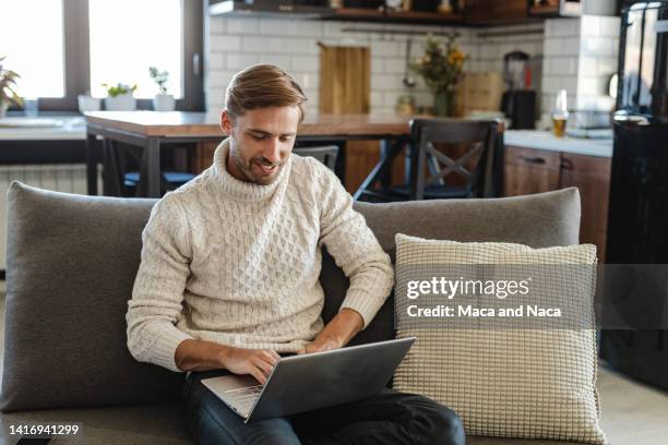 young man sitting on the sofa and connecting with people. - man sweater stockfoto's en -beelden