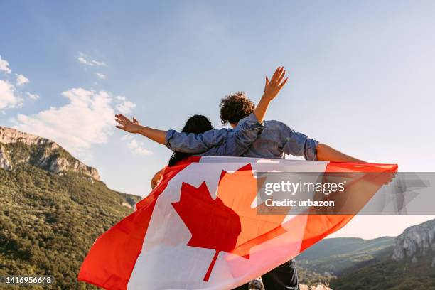 young couple waving a canadian flag at the top of the mountain - canada day stock pictures, royalty-free photos & images