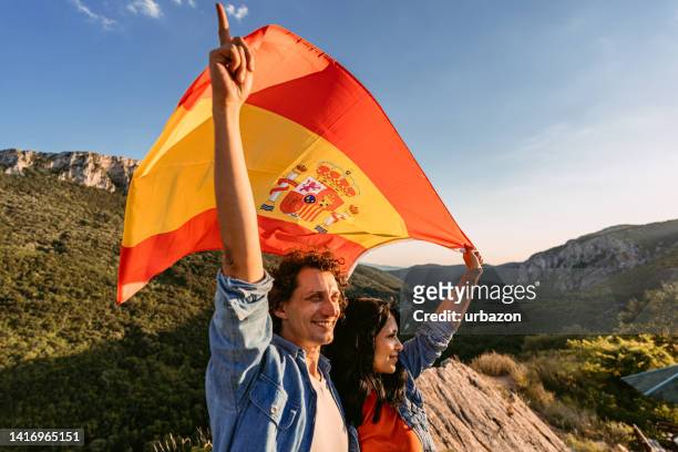 junges paar, das eine spanische flagge auf dem gipfel des berges schwenkt - spanische flagge stock-fotos und bilder