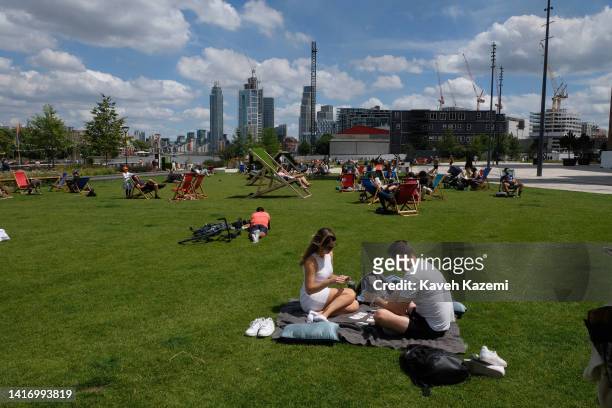 Couple play cards while sat on the grass on a sunny day outside Battersea Power Station which is one of the world's largest brick buildings on June...