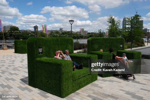 People relax on a sunny day while sat on a sofa made with artificial greens outside Battersea Power Station which is one of the world's largest brick...