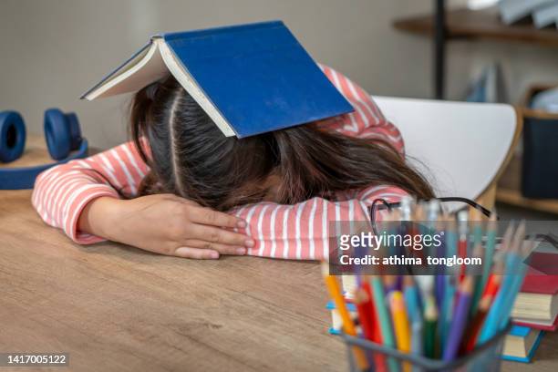 close up of a little girl sleeping on the table with a book on her head after reading and tired exhausted. - killing time stock pictures, royalty-free photos & images