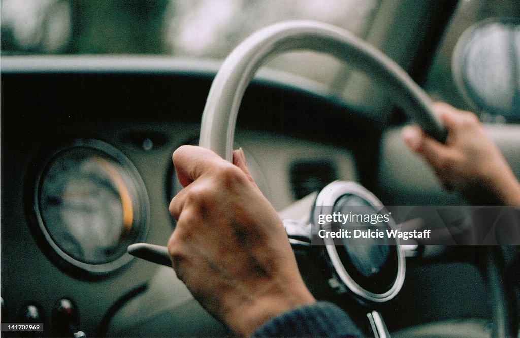 Veined hands driving vintage figaro car.