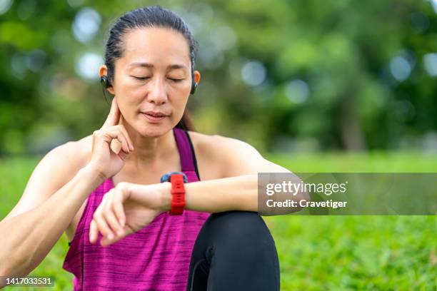 asian women take their pulse and read data on a smartwatch after running outdoors at a public park. outdoor exercise concepts.measurement heart rate in health technology. - taking pulse bildbanksfoton och bilder