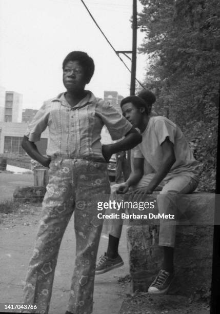 View of an unidentified woman as she stands, hands on her hips, on a sidewalk, Atlanta, Georgia, April 1970. Several people are visible on a low wall...