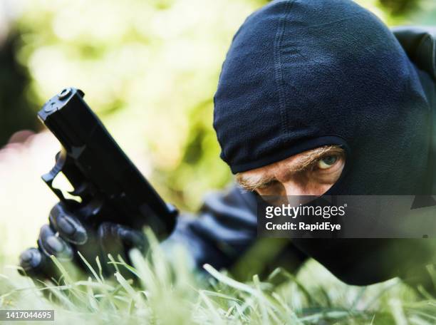 gunman wearing balaclava, assassin, burglar or secret agent, frowns at the camera as he holds a semiautomatic pistol - rob cross stock pictures, royalty-free photos & images