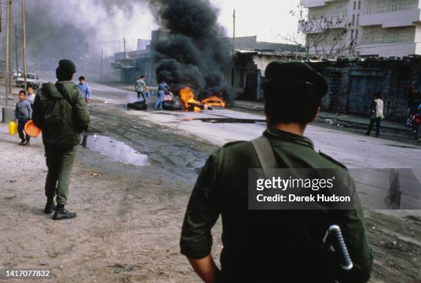 View, past a pair of uniformed soldiers, of a pile of burning tires on an unspecified street during the First Palestinian Intifada, Gaza, Palestine,...