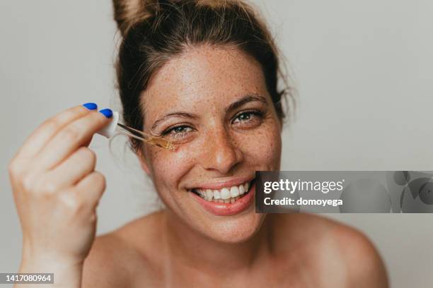 happy young freckled woman applying face serum - faces freckles stockfoto's en -beelden