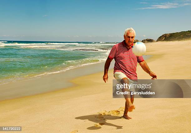 65 year old man playing with ball on a beach - senior kicking stock pictures, royalty-free photos & images