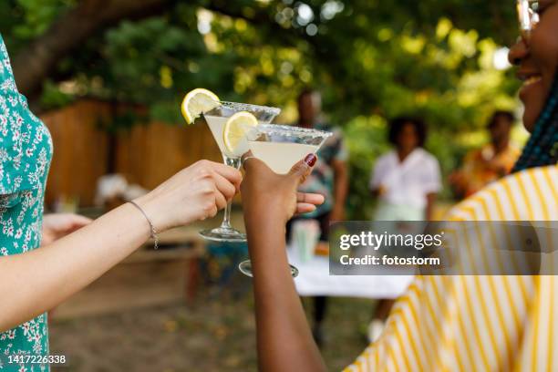 two girlfriends cheering with martini glasses with margarita cocktails - summer cocktails garden party drinks stockfoto's en -beelden