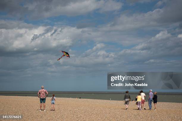 An adult and child fly a kite as people walk on the pebble beach on August 20, 2022 in Aldeburgh, England .