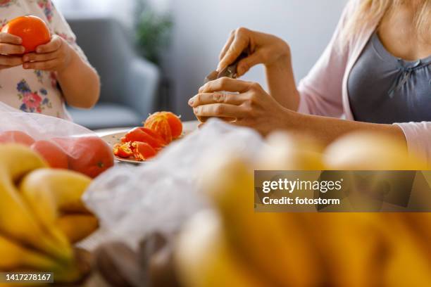 woman cutting up a kiwi fruit, her little daughter assisting her by peeling tangerines - cutting green apple stock pictures, royalty-free photos & images