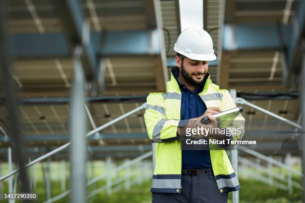 solar power monitoring system in field operation. a male solar site engineer uses a tablet computer by a mobile app to track solar panel devices to monitor the sun's radiation to convert the energy of light directly into electricity. - regular guy stock pictures, royalty-free photos & images