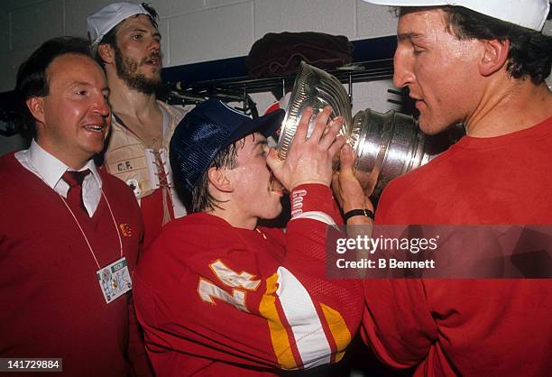 Theoren Fleury of the Calgary Flames drinks champagne from the Stanley Cup Trophy as his teammate Tim Hunter helps him hold the Cup after the Flames...