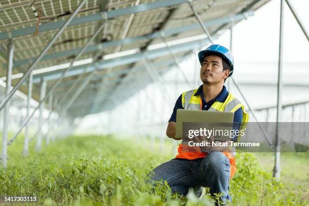 increase solar power production and performance by using cloud-based monitoring. solar service technician use a laptop computer under a solar panels module to access logs data of equipment to troubleshoot in a solar power plant. - carbon neutrality stockfoto's en -beelden