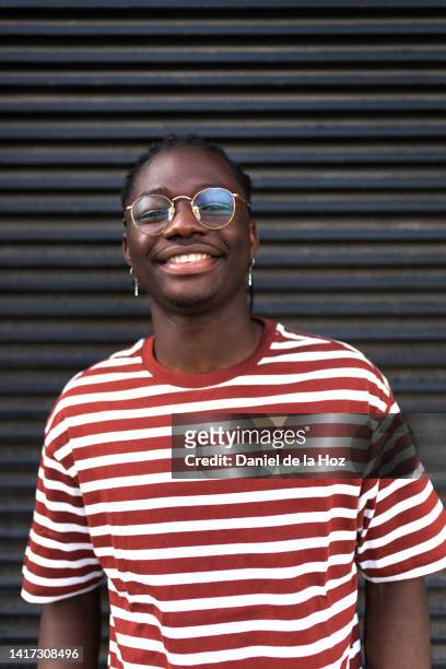 portrait of happy smiling african american young man looking at camera wearing stripped t-shirt and glasses. dark background. vertical image. - black t shirt stock pictures, royalty-free photos & images