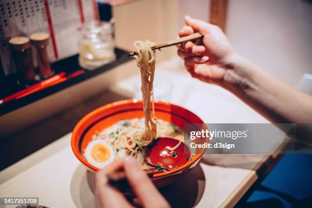 cropped hand of woman eating a bowl of freshly served traditional japanese ramen with chopsticks in a japanese restaurant. asian cuisine and food culture. eating out lifestyle - food styling soup stock pictures, royalty-free photos & images